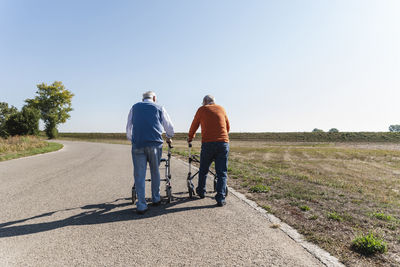 Two old friends walking on a country road, using wheeled walkers