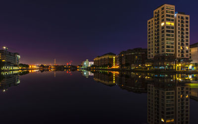 Illuminated buildings reflecting in lake against clear sky at dusk