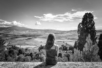 Rear view of young woman sitting on retaining wall at val d orcia