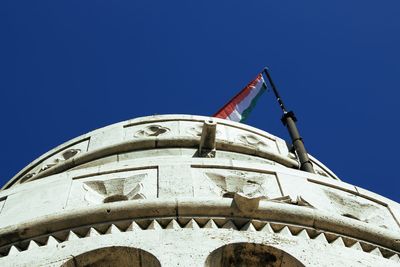 Low angle view of flags on building against clear blue sky