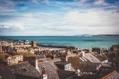 High angle view of city scape against sea and cloudy sky