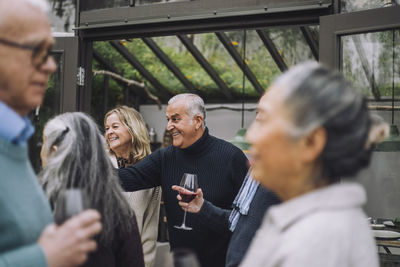 Happy mature man enjoying with senior male and female friends during dinner party at backyard