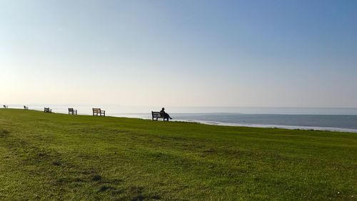 Person sitting on park bench by sea against sky