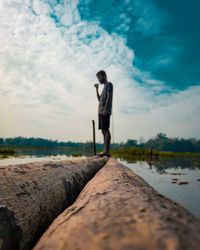 Full length of man standing on log amidst lake against sky