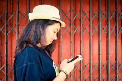 Portrait of young woman using mobile phone while standing by fence