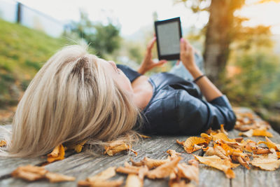 Woman using digital tablet while lying on bench during autumn