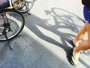 Low section of woman walking on footpath by bicycle