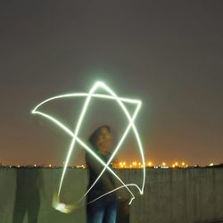 Man standing by illuminated lights against sky at night