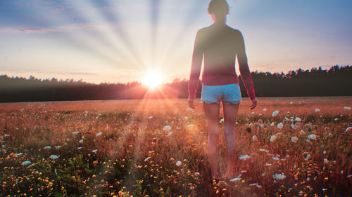 Rear view of woman levitating on plants over field during sunset