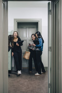 Full length of cheerful female students in corridor at school