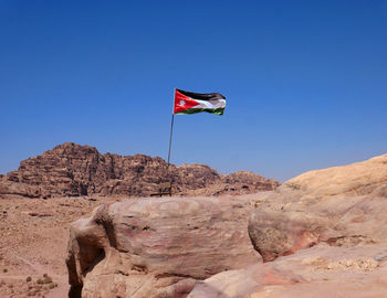 Low angle view of flag on rock against blue sky