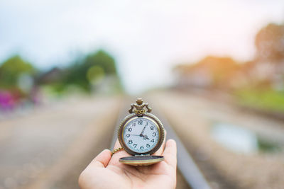 Close-up of hand holding clock against blurred background