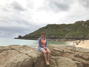 Portrait of woman sitting on rock by sea against sky