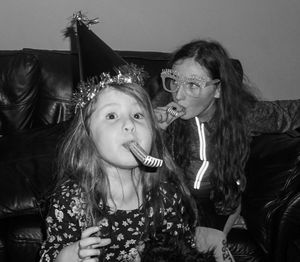 Sisters blowing party horn blowers while sitting at home