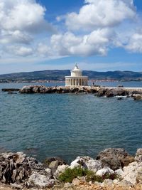 Lighthouse on beach against cloudy sky