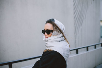 Low angle view of woman wearing sunglasses standing against wall