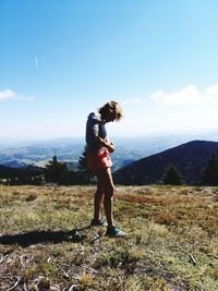 Woman adjusting hot pants while standing on field against sky