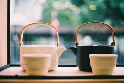 Close-up of cups and tea kettles in tray against window