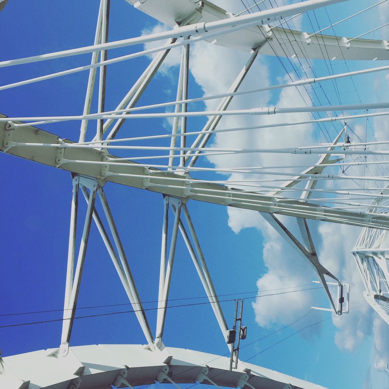 low angle view, blue, sky, built structure, architecture, metal, day, fuel and power generation, sunlight, clear sky, no people, directly below, part of, outdoors, electricity, connection, technology, hanging, power line, metallic