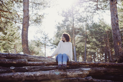 Rear view of woman sitting on tree trunk in forest