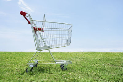 Shopping cart on field against sky