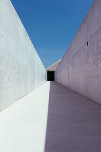 Alley amidst concrete wall against blue sky during sunny day