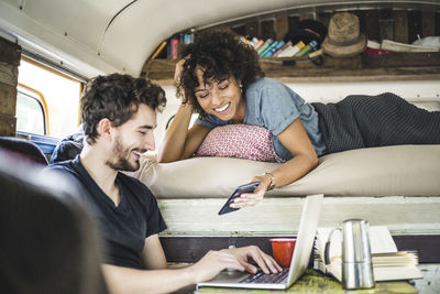 Happy young woman showing mobile phone to man sitting with laptop in motor home