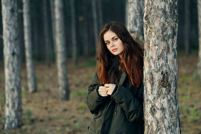 Portrait of woman standing by tree trunk in forest