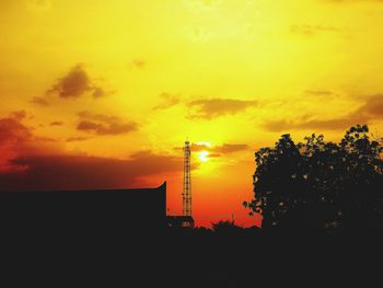 Silhouette of factory against orange sky