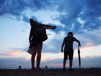 Friends standing on beach against sky during sunset