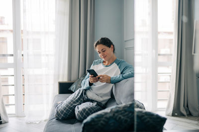 Young woman using laptop while sitting on bed at home