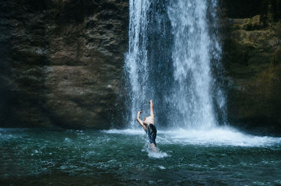 Man splashing water while jumping by waterfall