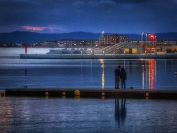 Illuminated standing by river against sky in city at night