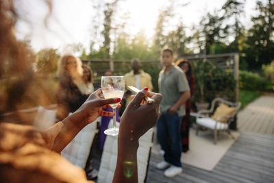 Woman holding drink glass while hosting dinner party with friends in back yard