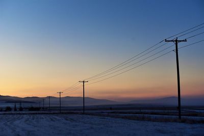 Electricity pylons against clear sky during sunset