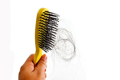 Cropped hand holding hairbrush with messy hair against white background