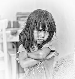 Sad girl with arms crossed standing against wall at home