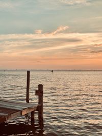 Wooden posts in sea against sky during sunset