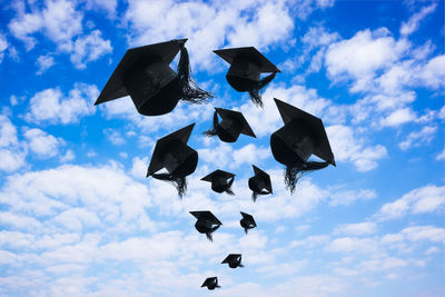 Low angle view of mortarboards flying against blue sky