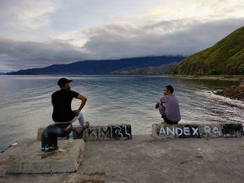 Rear view of men sitting on lake against sky