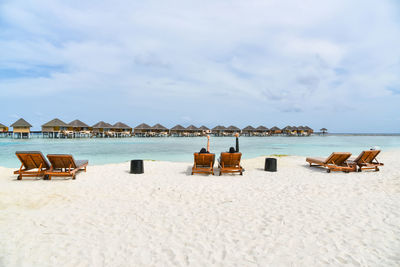 Deck chairs on beach against sky