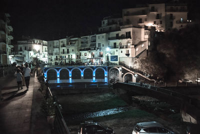 People on illuminated bridge in city at night