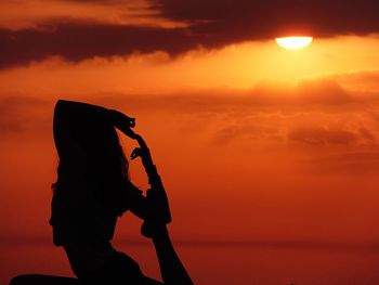 Silhouette woman exercising orange sky during sunset