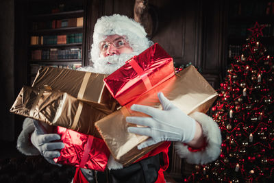 Man wearing santa claus costume holding christmas presents at home