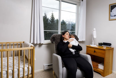 A mother holds her baby over her shoulder and rocks in a rocking chair