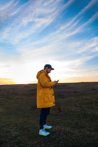 Traveler man in yellow coat with smartphone walking on a hill sunset sky  authentic male with gadget