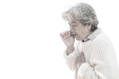 Close-up of senior woman coughing against white background