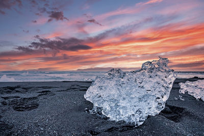 Beautiful ice crystal on black sand of diamond beach against cloudy sky at sunset