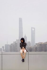 Woman standing by modern buildings in city against sky