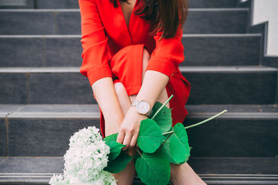 Midsection of woman holding flowers while sitting on steps